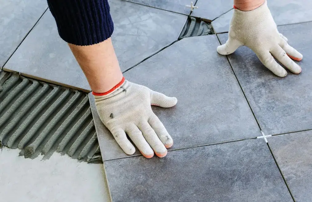 Oficial colocando baldosas grandes de gres en suelo de vivienda con adhesivo en Huelva