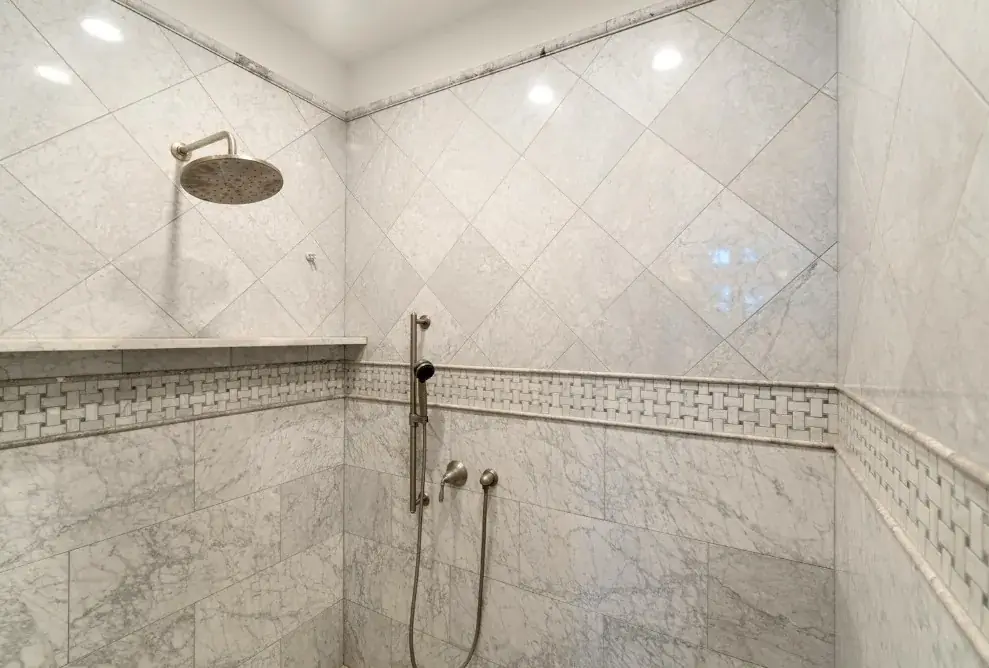 Ducha de mármol blanco con alicatado en diagonal y cenefa decorativa en Huelva