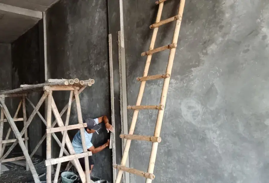 Albañil enluciendo una pared interior con mortero desde andamio